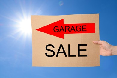 Image of Woman holding sign with text GARAGE SALE against blue sky