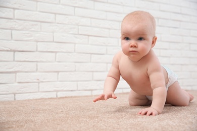 Cute little baby crawling on carpet near brick wall, space for text