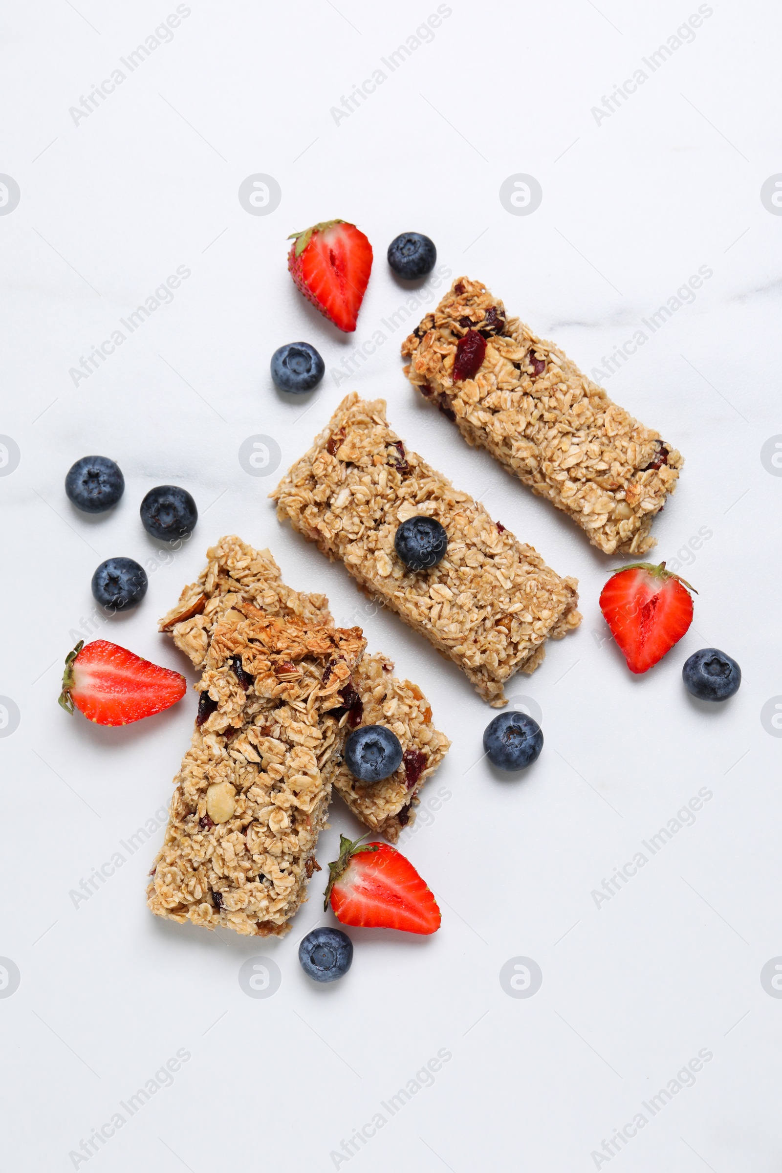 Photo of Tasty granola bars and berries on white marble table, flat lay