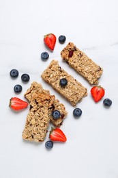 Photo of Tasty granola bars and berries on white marble table, flat lay