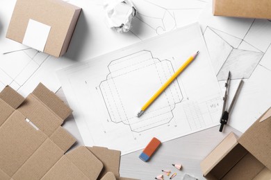 Photo of Creating packaging design. Drawings, boxes and stationery on light wooden table, flat lay