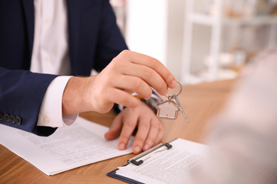 Photo of Real estate agent giving key with trinket to client in office, closeup