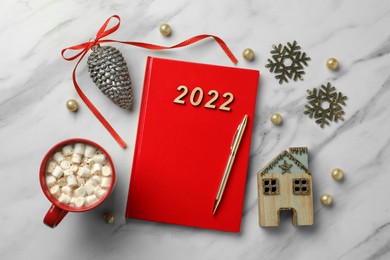 Red planner, cup of tasty hot drink and Christmas decor on white marble background, flat lay. 2022 New Year aims