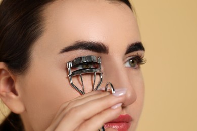 Woman using eyelash curler on beige background, closeup