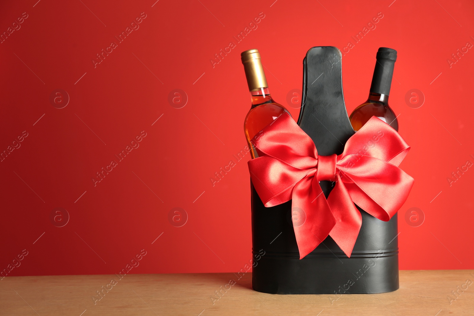 Photo of Bottles of wine in holder with bow on table against color background. Space for text