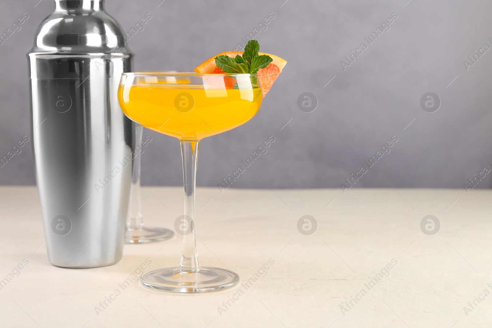 Photo of Delicious cocktail and metal shaker on light table, space for text