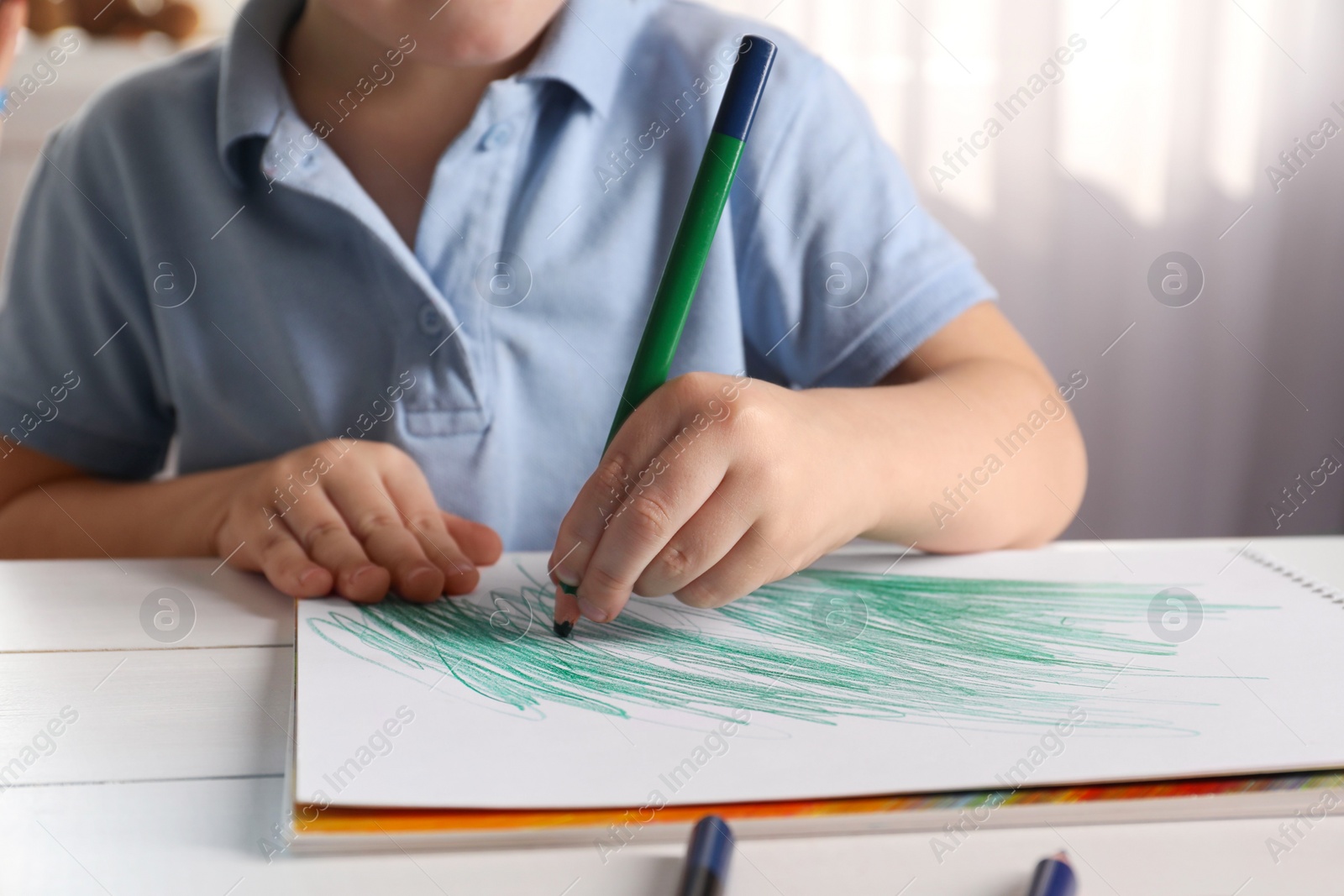 Photo of Little boy drawing with pencil at white wooden table indoors, closeup. Child`s art