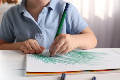 Little boy drawing with pencil at white wooden table indoors, closeup. Child`s art