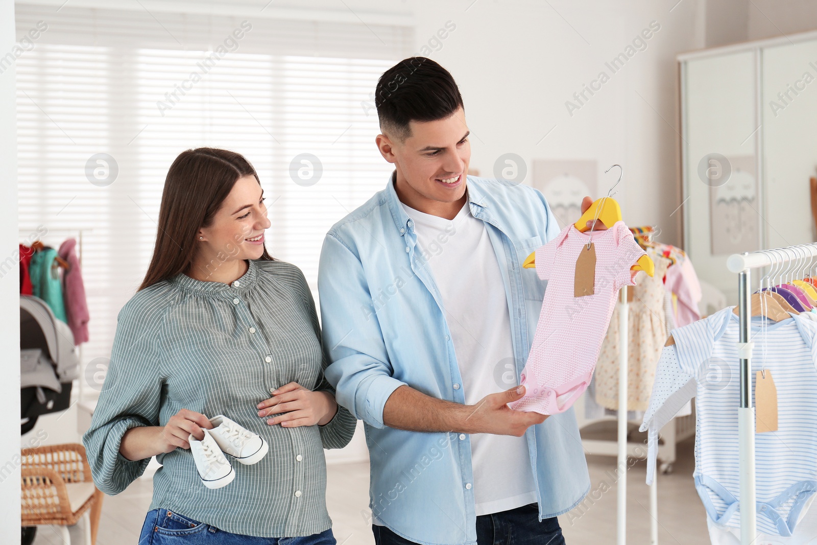 Photo of Happy pregnant woman with her husband choosing baby clothes and shoes in store. Shopping concept