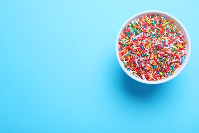 Photo of Colorful sprinkles in bowl on light blue background, top view with space for text. Confectionery decor