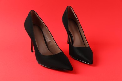 Photo of Pair of elegant black high heel shoes on red background