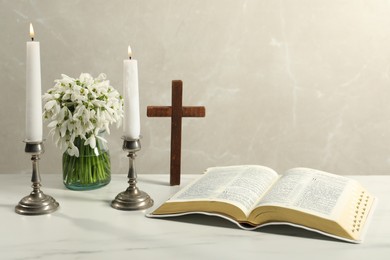 Burning church candles, Bible, wooden cross and flowers on white marble table