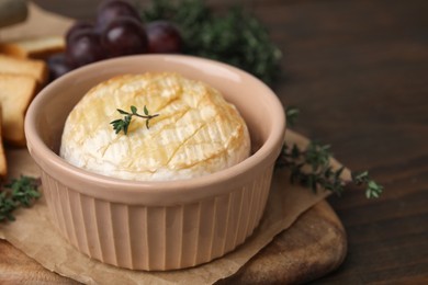 Photo of Tasty baked camembert in bowl on wooden table, closeup