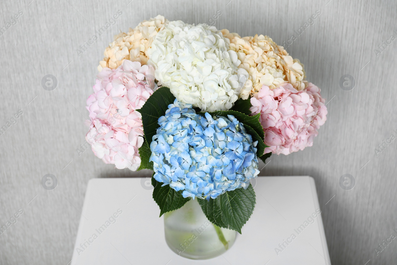 Photo of Beautiful hydrangea flowers in vase on white bedside table near light gray wall, closeup