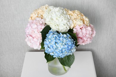 Photo of Beautiful hydrangea flowers in vase on white bedside table near light gray wall, closeup