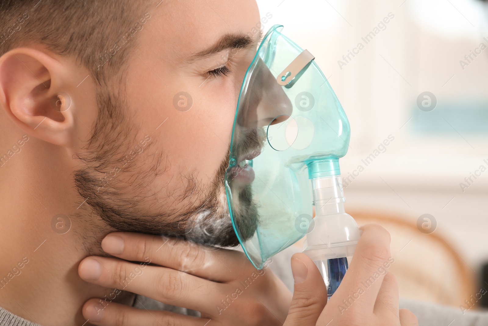 Photo of Sick man using nebulizer for inhalation indoors, closeup