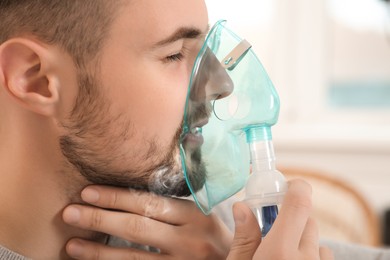 Photo of Sick man using nebulizer for inhalation indoors, closeup