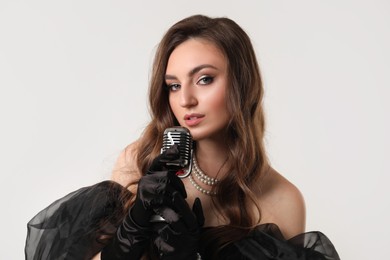 Beautiful young woman with microphone singing on light grey background