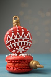 Photo of Beautifully decorated Christmas macarons on light blue wooden table against blurred festive lights, closeup