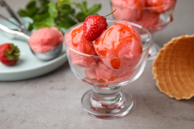 Photo of Delicious pink ice cream served with syrup and strawberry in dessert bowl on grey table