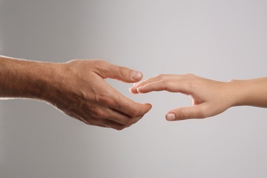 Man reaching for woman's hand on grey background, closeup. Help and support concept