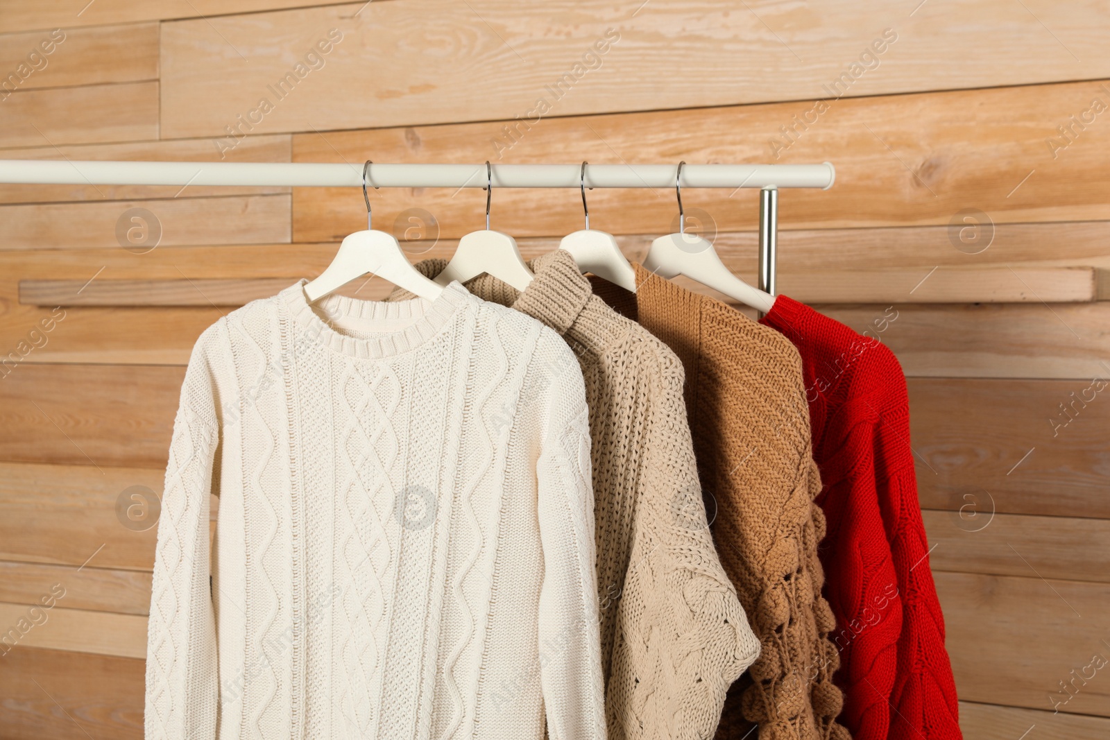 Photo of Collection of warm sweaters hanging on rack against wooden background