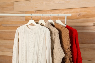 Collection of warm sweaters hanging on rack against wooden background