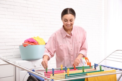 Young woman hanging clean laundry on drying rack indoors