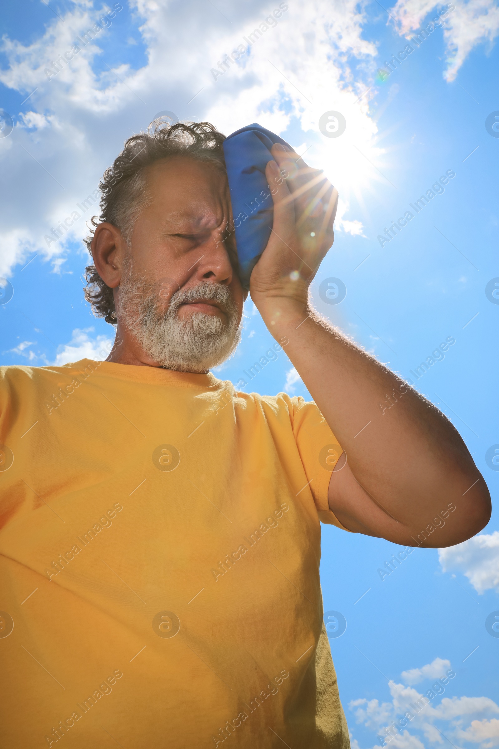 Photo of Senior man with cold pack suffering from heat stroke outdoors, low angle view