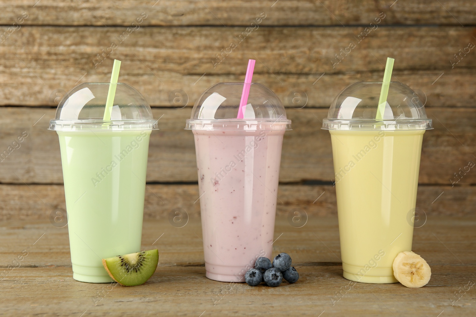 Photo of Plastic cups with different tasty smoothies and fresh fruits on wooden table