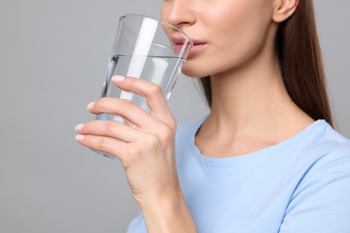 Photo of Healthy habit. Woman drinking fresh water from glass on grey background, closeup