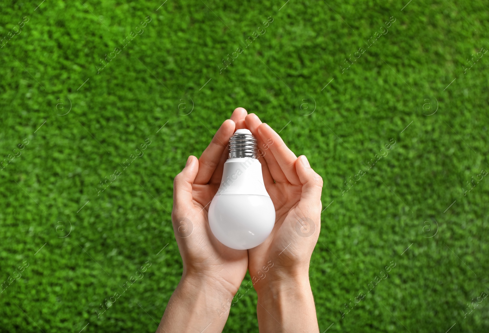 Photo of Woman holding LED light bulb over green grass, top view