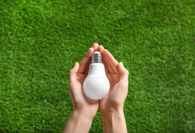 Photo of Woman holding LED light bulb over green grass, top view