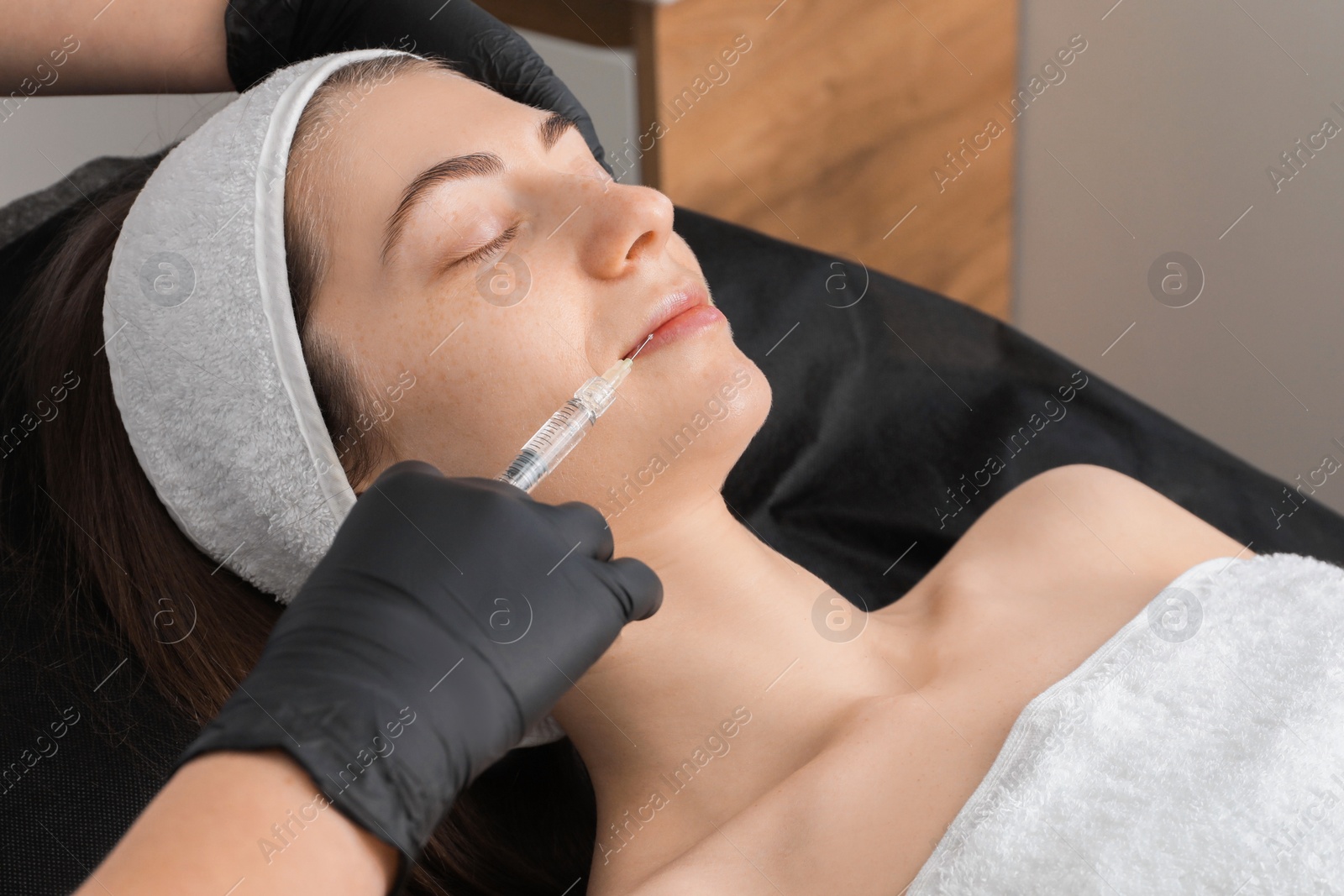 Photo of Cosmetologist giving lips injection to patient in clinic, closeup. Cosmetic surgery