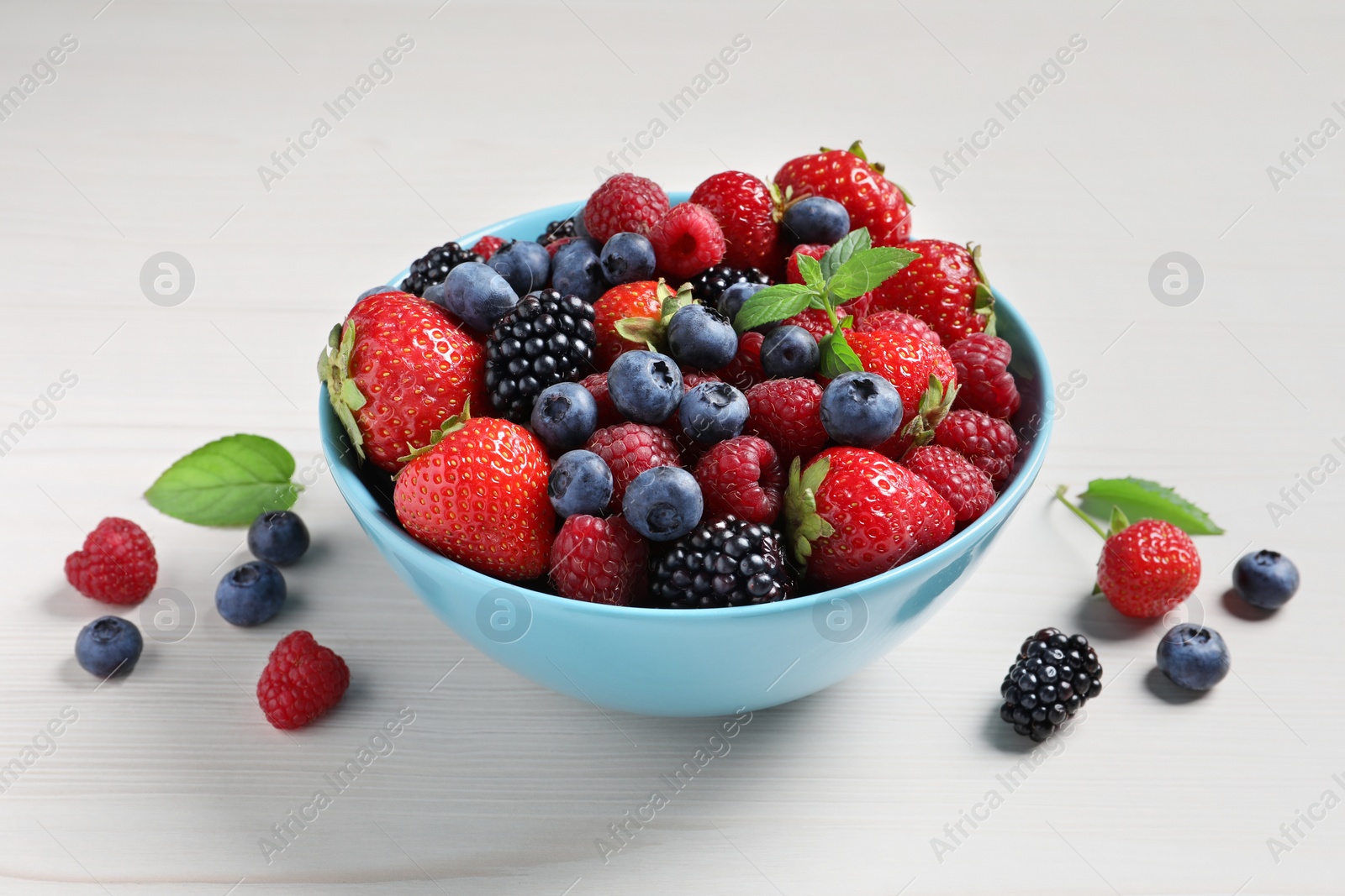 Photo of Many different fresh ripe berries in bowl on white wooden table