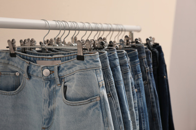 Rack with stylish jeans on color background, closeup