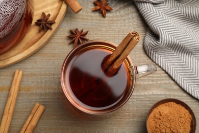 Glass cup of hot tea with aromatic cinnamon on wooden table, flat lay