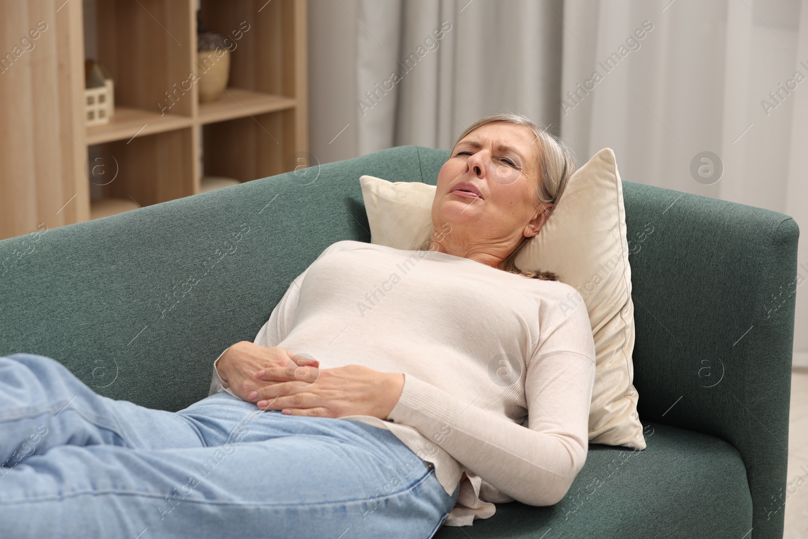 Photo of Menopause. Woman suffering from abdominal pain on sofa at home