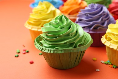 Photo of Delicious bright cupcakes and sprinkles on coral background, closeup