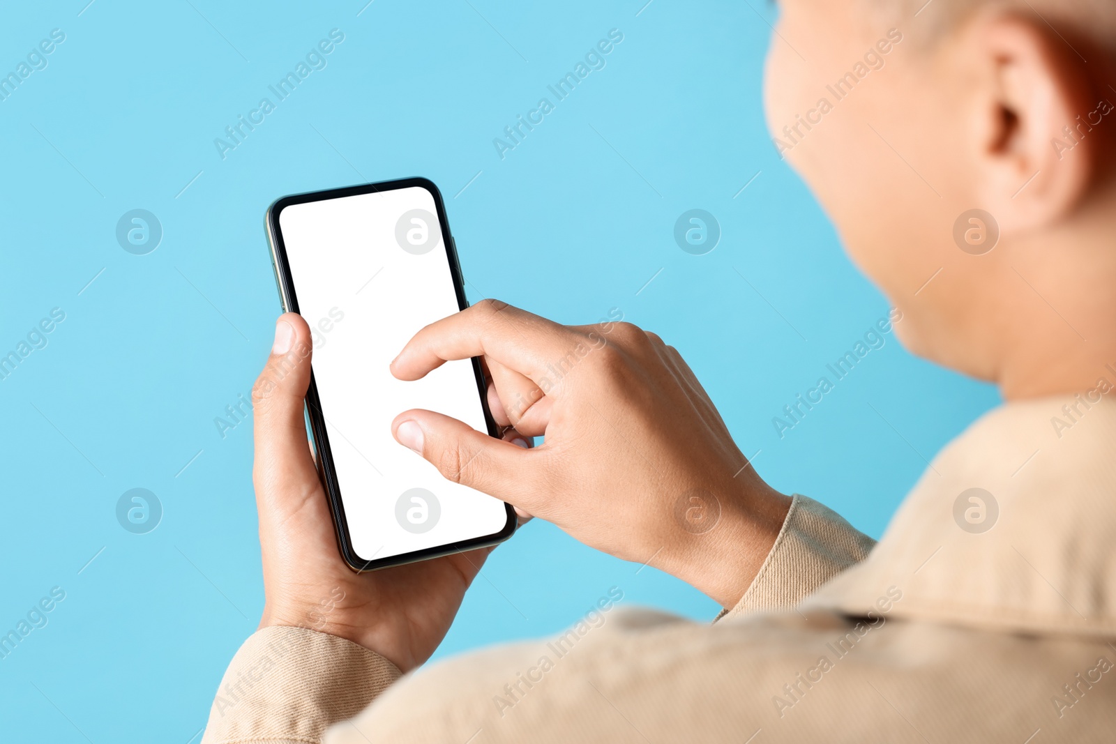 Photo of Young man using smartphone with blank screen on light blue background, closeup. Mockup for design