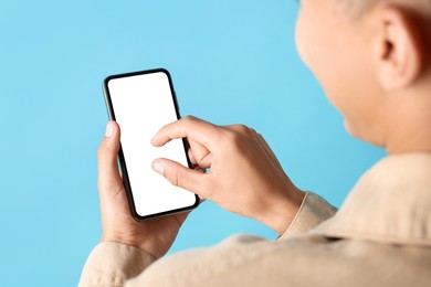 Young man using smartphone with blank screen on light blue background, closeup. Mockup for design