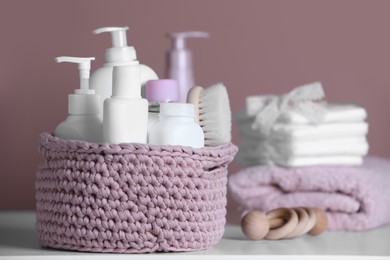 Photo of Baby cosmetic products and hair brush in knitted basket on white table. Space for text