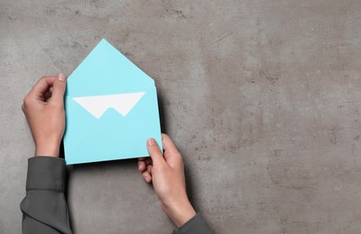 Photo of Woman holding letter envelope with card at grey textured table, top view. Space for text