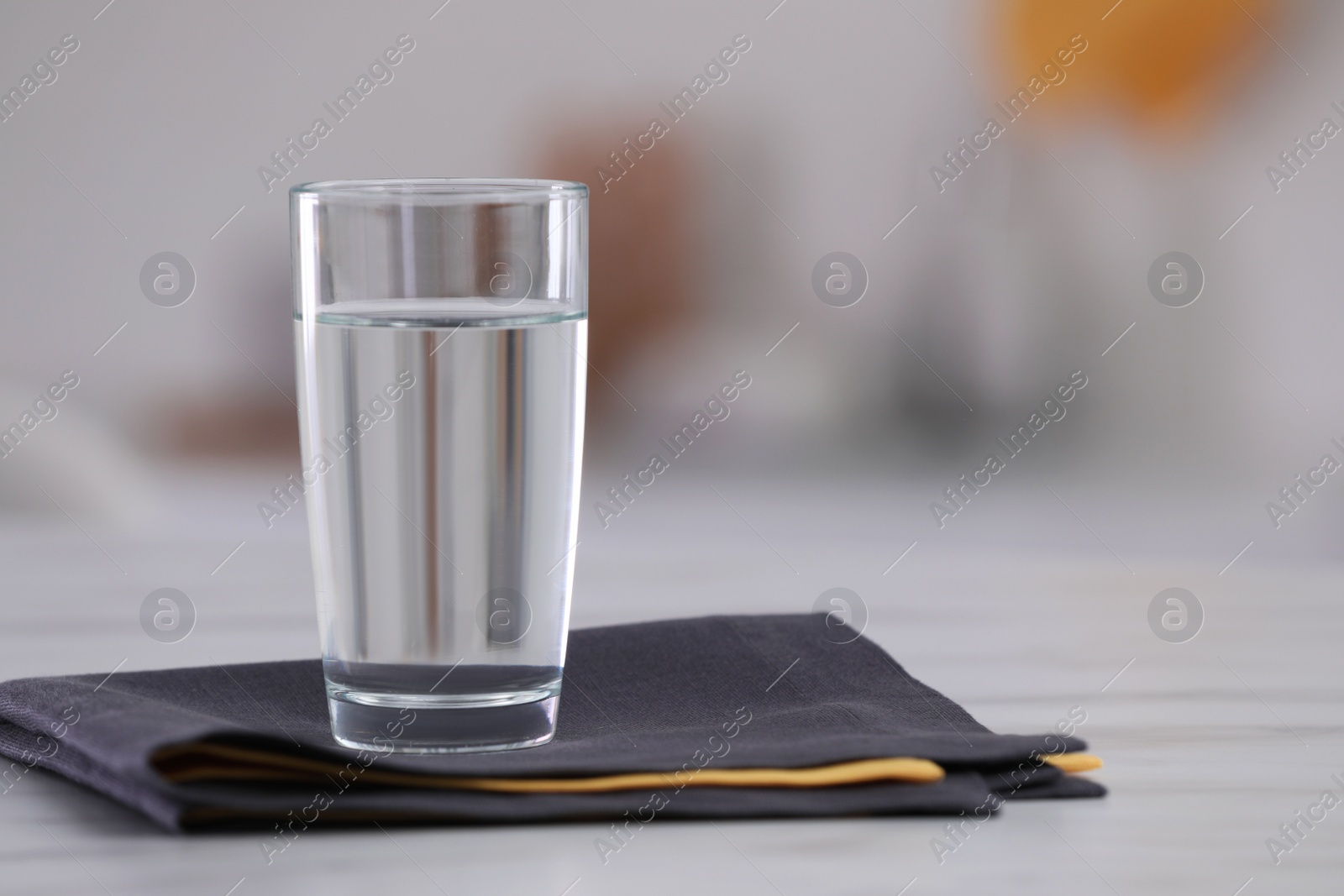 Photo of Glass of water and napkins on white table against blurred background. Space for text