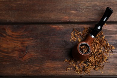 Photo of Smoking pipe and dry tobacco on wooden table, flat lay. Space for text
