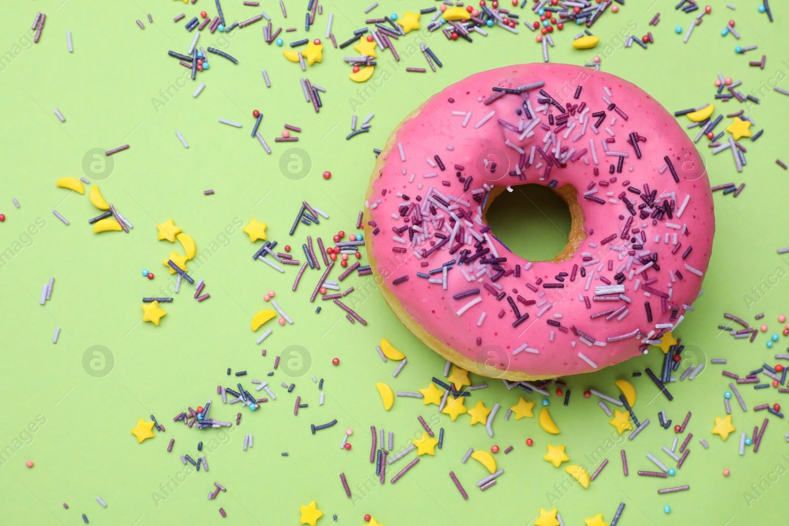 Photo of Glazed donut decorated with sprinkles on green background, flat lay. Space for text. Tasty confectionery