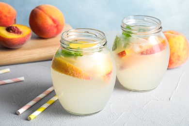 Photo of Tasty peach cocktail in glass jars on table. Refreshing drink