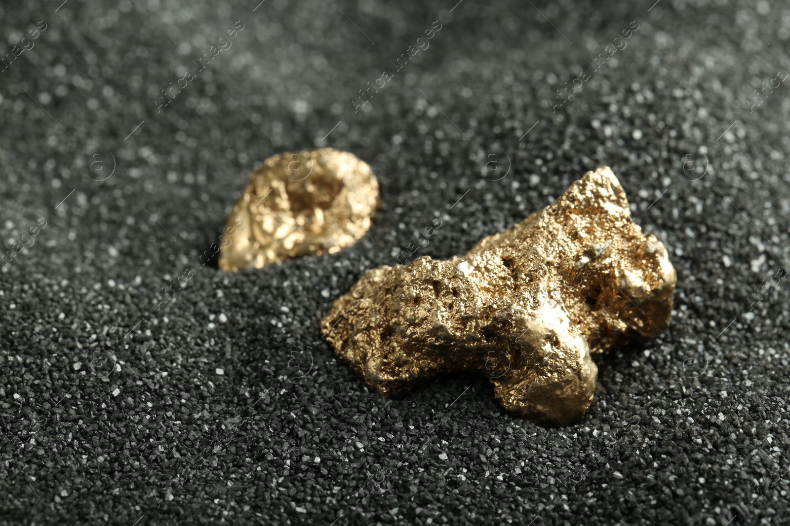 Photo of Shiny gold nuggets on black sand, closeup