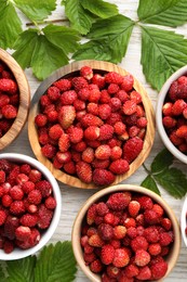 Photo of Fresh wild strawberries in bowls and leaves on white wooden table, flat lay