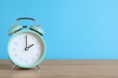 Photo of Turquoise alarm clock on wooden table against light blue background, space for text